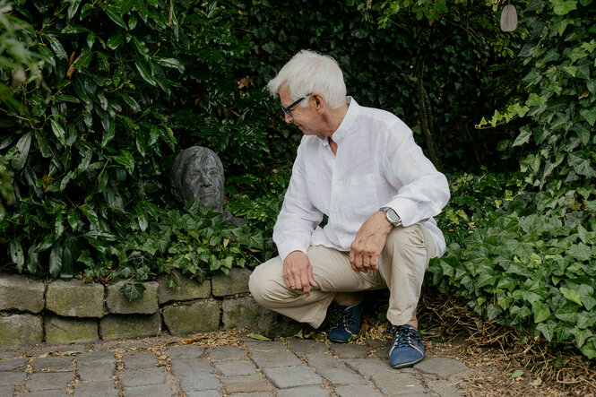 Ein Mann kniet auf dem Boden und schaut sich eine büste an, die ihn selbst darstellt
