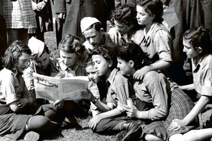 Eine historische Aufnahme zeigt junge Leute, die eine Zeitung lesen