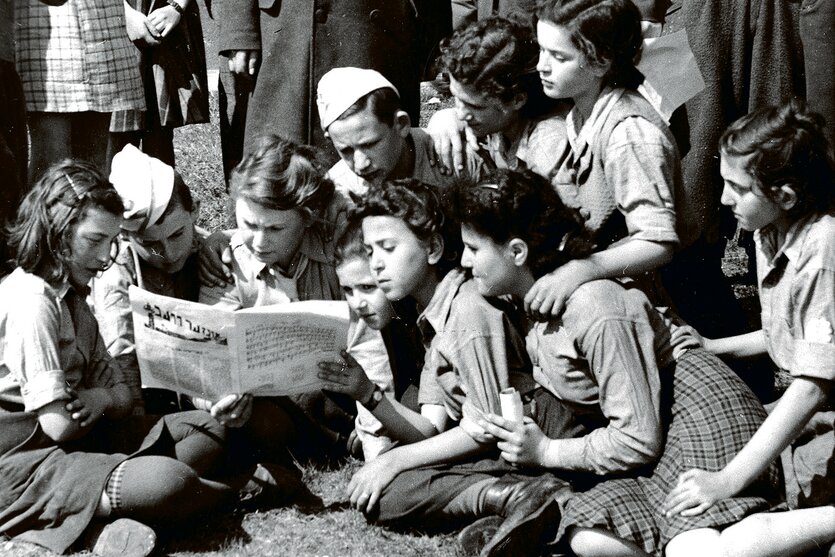 Eine historische Aufnahme zeigt junge Leute, die eine Zeitung lesen
