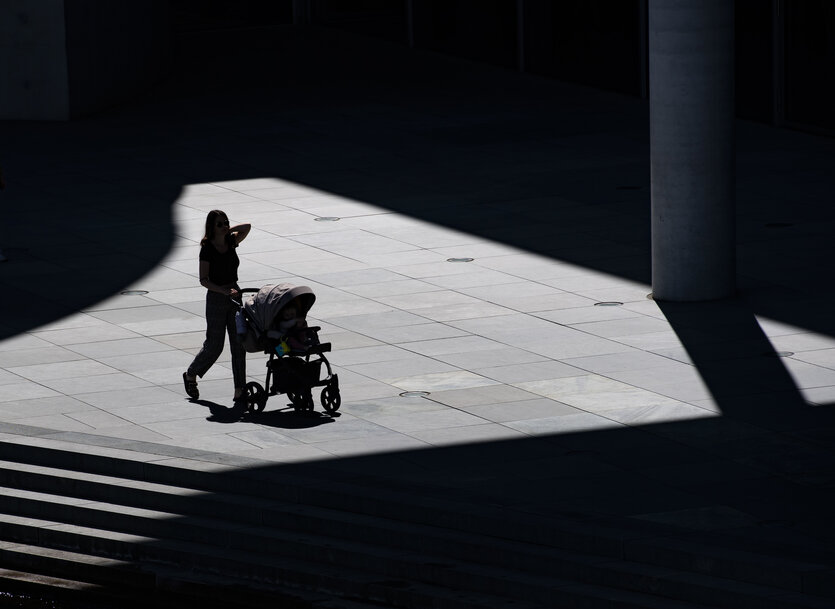 Nur als Silhouette ist eine Frau zu erkennen, die mit einem Kinderwagen spazieren geht.