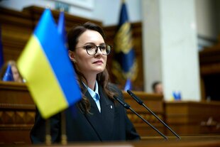 Poreträt von Yuliia Svyrydenko, sie steht im Parlament, eine ukrainische Flagge steht vor ihr