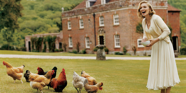 Madonna steht vor einem englischen Landhaus und füttert Hühner.