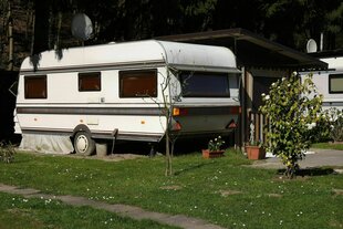Ein Wohnwagen steht auf der Wiese eines Campingplatzes, Blumenkästen und kleine Büsche davor