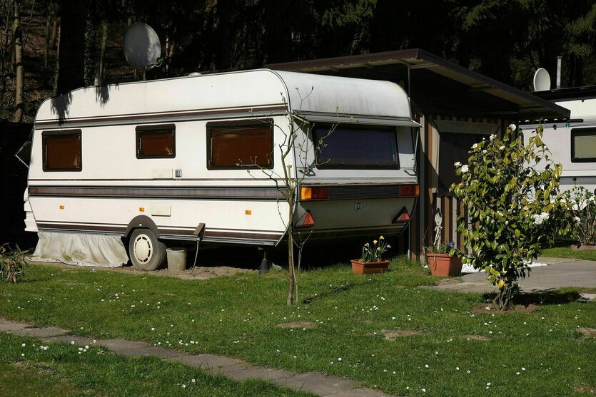 Ein Wohnwagen steht auf der Wiese eines Campingplatzes, Blumenkästen und kleine Büsche davor