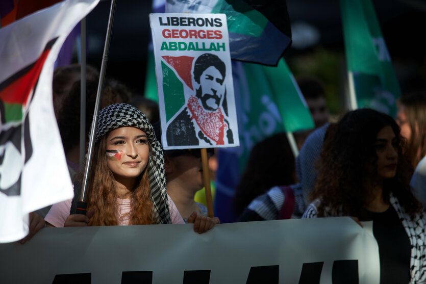 Eine Frau mit Palästinensertuch trägt ein Schild mit der Aufschrift "Liberons Geroges Abdallah"