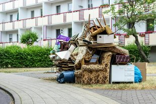 Vor einem Mehrfamilienhaus mit Balkonen steht eine Wohnungseinrichtung auf der Straße. Besonders markant sind die gemusterten Sessel