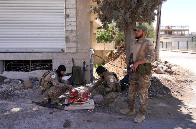 Soldaten machen Pause, einer hält Wache, die beiden anderen zerschneiden ein Wassermelone am Rande von verlassenen Gebäuden