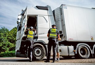 Zwei Menschen in Polizeiuniform kontrollieren einen weißen LKW