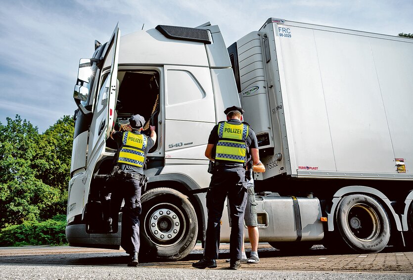 Zwei Menschen in Polizeiuniform kontrollieren einen weißen LKW