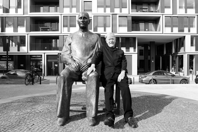 Claus Peymann neben einem Denkmal von Bertholt Brecht.