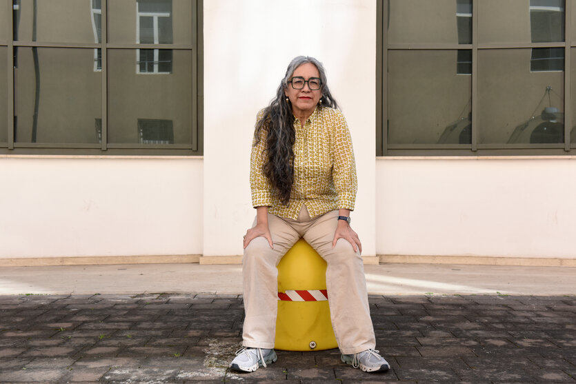 Eine Frau sitzt auf einem Poller und schaut direkt in die Kamera