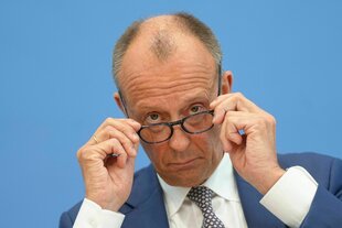 Kanzler Merz fasst sich an seine Brille.