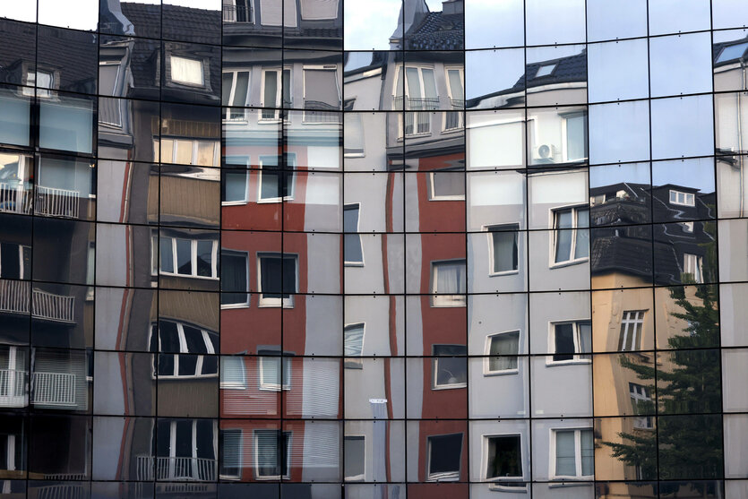 In einer Fassade spiegeln sich Mehrfamilienhäuser.