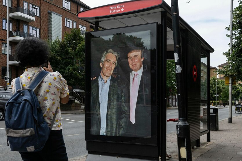 Die kurze Seite einer Bushaltestelle. Dort hängt an dem Ort, an dem sonst Werbeplakate hängen, ein riesiges Bild von Epstein und Trump, die in Anzug eng nebeneinanderstehen. Ein Mensch steht vor dem Plakat und schaut es an und macht ein Foto mit seinem Handy.