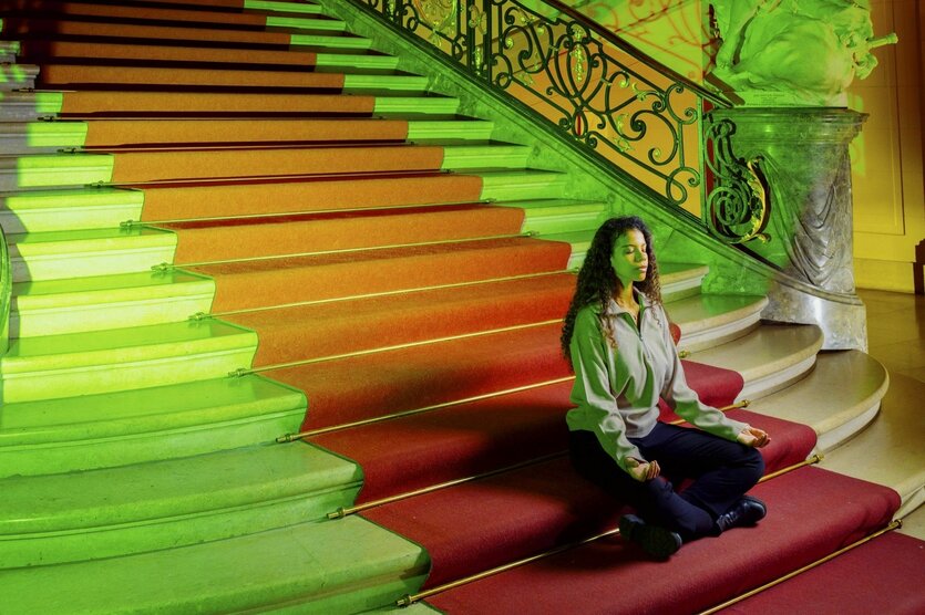 Eine Frau sitzt im Schneidersitz auf einer Treppe des Bode-Museums und meditiert