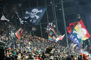 Im Millerntorstadion feiern Fans von St. Pauli beim Einlauf der Mannschaften und schwenken Fahnen.