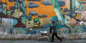 Ein Mann schiebt einen Einkaufswagen vor einem Grafitti entlang