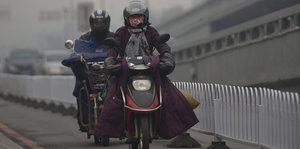 Motorradfahrer mit Mundschutz vor vernebelter Stadtsilhouette