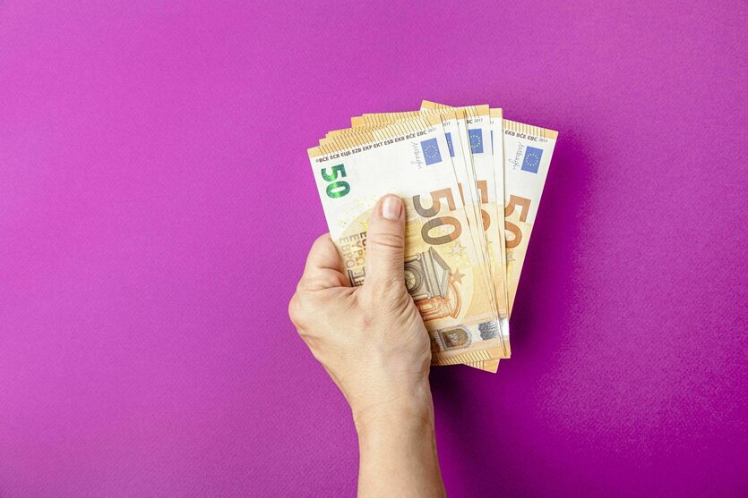 Eine Person hält ein Bündel von 50 Euro-Scheinen auf lila Hintergrund