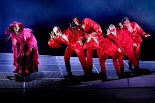 Auf einer blauen Bühne tanzt eine Gruppe von Schauspielerinnen in Rot