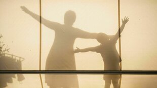 Ein Kind und eine Erwachsene Person werfen einen Schatten hinter einem Stoff.