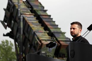 Selenskyj im Vordergrund, im Hintergrund ein Raketensystem mit Tarnmuster
