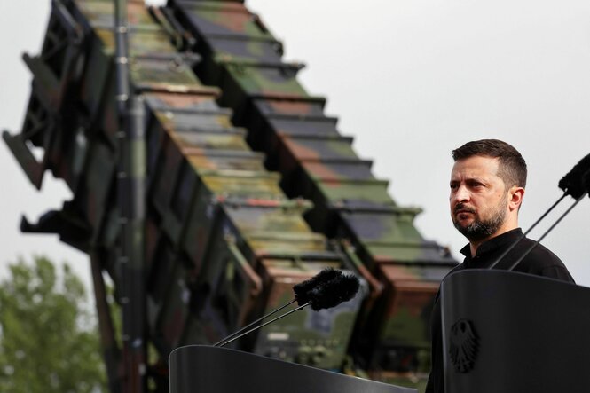Selenskyj im Vordergrund, im Hintergrund ein Raketensystem mit Tarnmuster