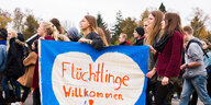 Frauen laufen durchs Bild mit einem großen Poster mit der Aufschrift "Flüchtlinge willkommen"