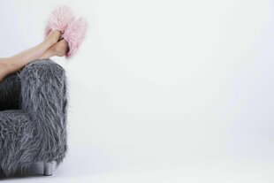 Ein graues Fellsofa auf dem Füße einer Frau in rosa Fellpuschen liegen