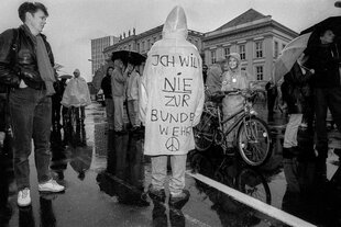 Demonstration gegen die Wehrpflicht - es regnet und auf dem Regenmantel eines jungen Mannes steht: Ich will NIE zur Bundeswehr