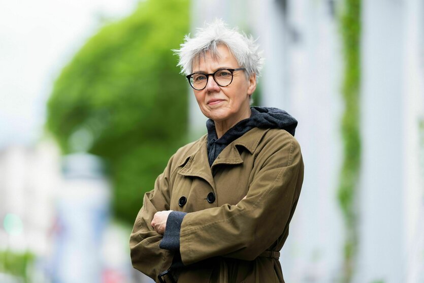 Frau mit kurzen weißen Haaren steht mit verschränkten Armen