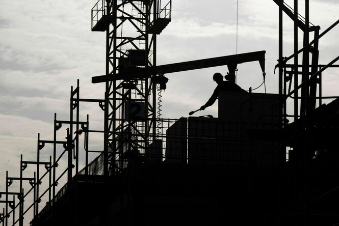 Ein Bauarbeiter arbeitet auf einer Baustelle, er trägt einen Helm - und von ihm und der Baustelle ist nur die Silhouette zu sehen
