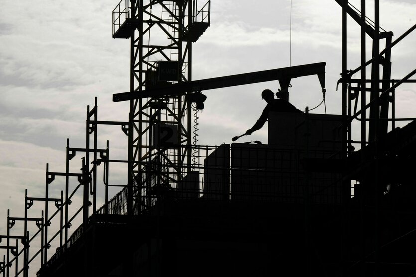 Ein Bauarbeiter arbeitet auf einer Baustelle, er trägt einen Helm - und von ihm und der Baustelle ist nur die Silhouette zu sehen