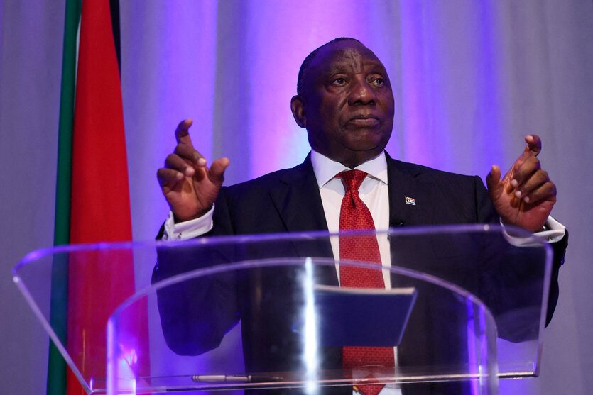 Cyril Ramaphosa steht an einem Rednerpult und hat die Arme gehoben, als ob er dirigieren wolle.