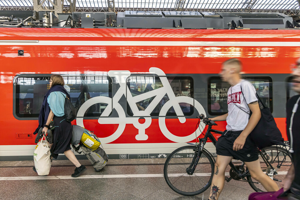Menschen mit Gepäck und Fahrrad laufen an einem Zug vorbei