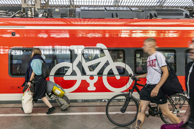 Menschen mit Gepäck und Fahrrad laufen an einem Zug vorbei