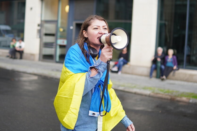 Eine protestierende Person mit einer ukrainischen Flagge um die Schulter gehängt ruft in ein Megafon
