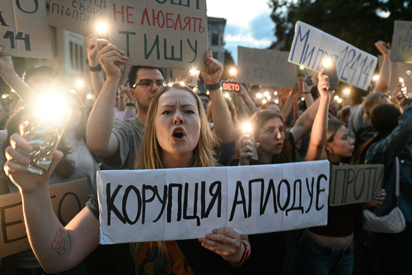 Eine Menge junger Personen verschiedner Geschelchter mit Schilder auf Ukrainisch, die Taschenlampe des Smartphones gezüvkt und erbost rufend