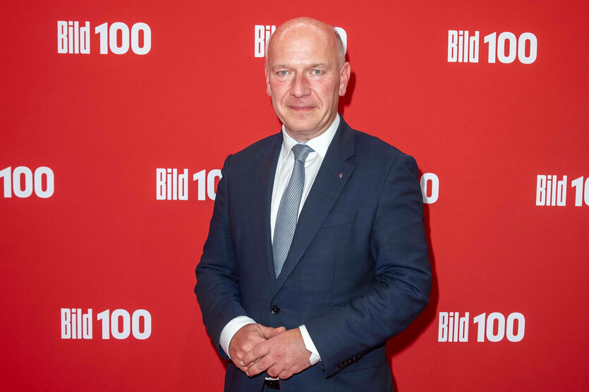 Mann steht vor roter Wand mit der Aufschrift Bild100