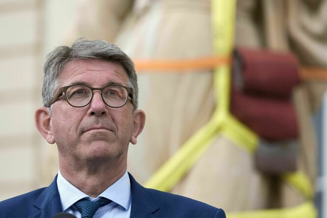 Wolfram Weimer nimmt an einer Pressekonferenz teil, im Hintergrund eine künstlerisch verpackte Skulptur, und blickt ausdrucklos in die Ferne