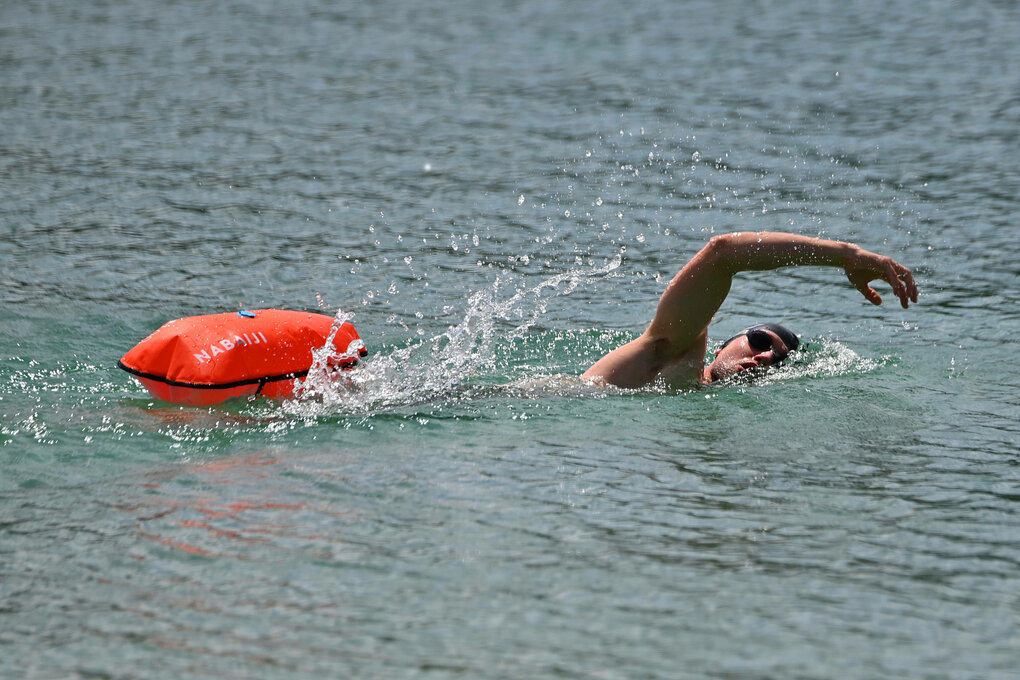 Mann schwimmt, krault im Wasser, eine Schwimm-Boje hinter sich