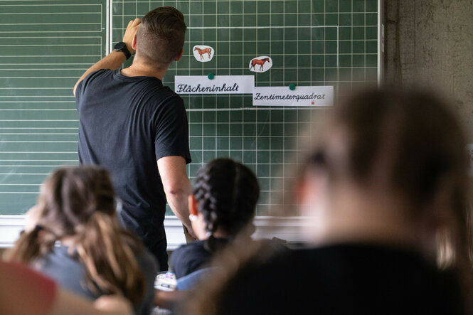 Lehrer schreibt im Unterricht etwas an eine Tafel.