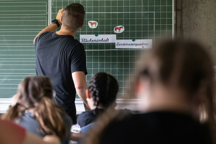 Lehrer schreibt im Unterricht etwas an eine Tafel.