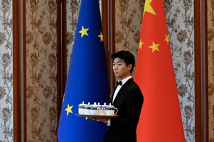 Eine Person mit einem Tablett vor einer EU und einer chinesischen Flagge.
