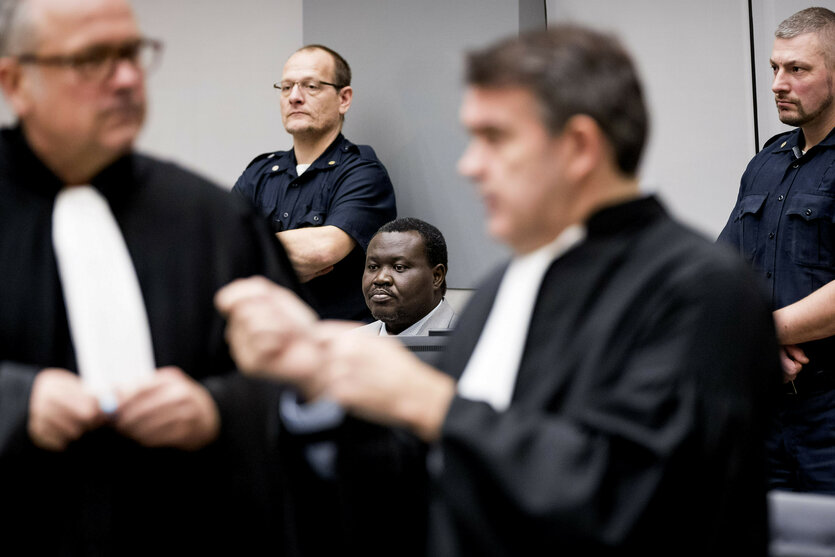 Ein Mann im Anzug, hinter ihm Beamte, im Vordergrund Männer in Richterroben