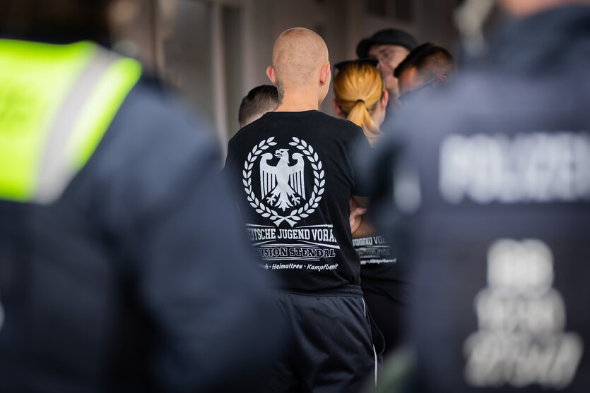 Junger Glatzkopf hinter Polizisten mit T-Shirt der "Deutschen Jugend Voran"