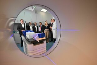 Blick aus einer Tomographen Röhre auf eine Gruppe Politikerinnnen, u.a. Die Gesundheitsministerin Warken und medizinisches Personal