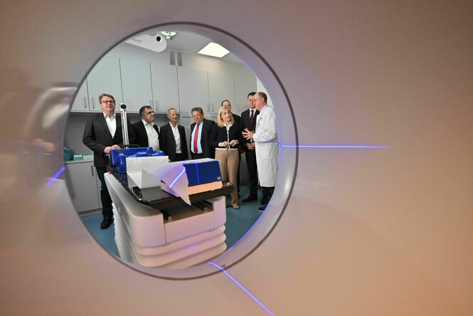Blick aus einer Tomographen Röhre auf eine Gruppe Politikerinnnen, u.a. Die Gesundheitsministerin Warken und medizinisches Personal