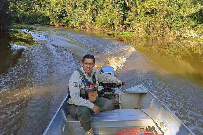 Ein Mann sitzt in Ranger-Uniform in einem Motorboot. Mit der linken Hand am Lenker, guckt er nach vorne und fährt einen Fluss entlang