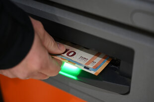 Eine Hand zieht Geldscheine aus einem Automaten